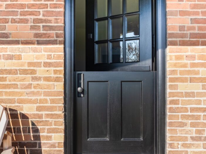 Exterior of a black Dutch door with the top half open, offering a peek into the cozy farmhouse interior.