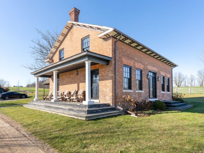 The front exterior of a modern farmhouse with large metal-clad wood windows, a welcoming porch, and a landscaped yard.
