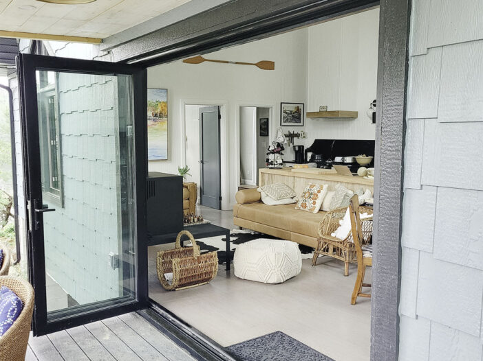 Black bi-folding patio doors fully open in a Muskoka cottage connecting the living space to the outdoor deck.