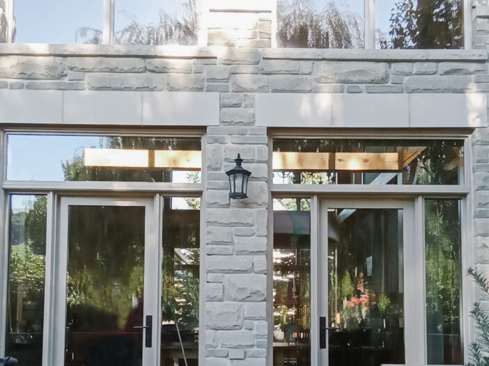 Custom wood-clad French doors installed on a Toronto home with stone exterior and transom windows above.